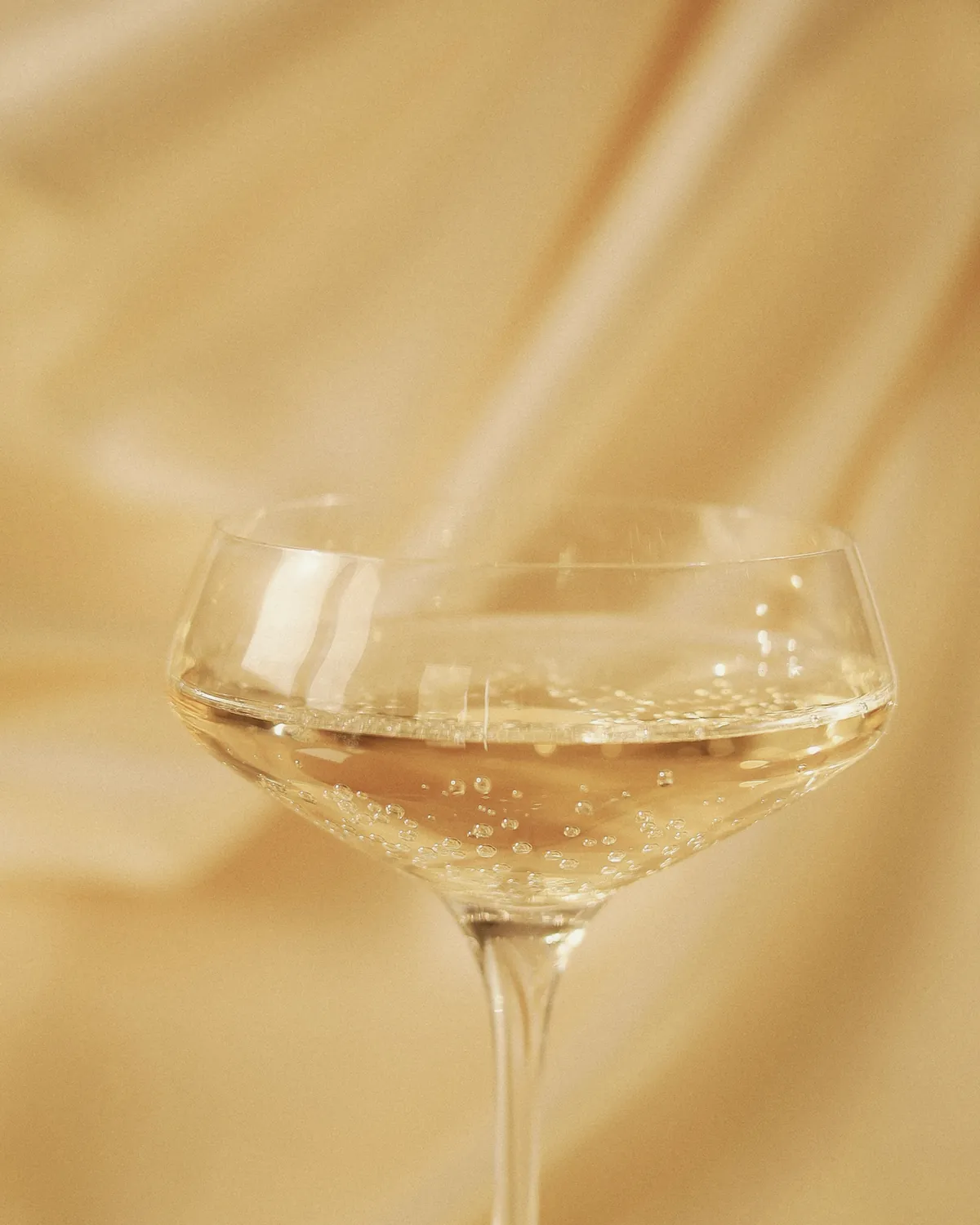 A coupe of sparkling wine against soft gold fabric